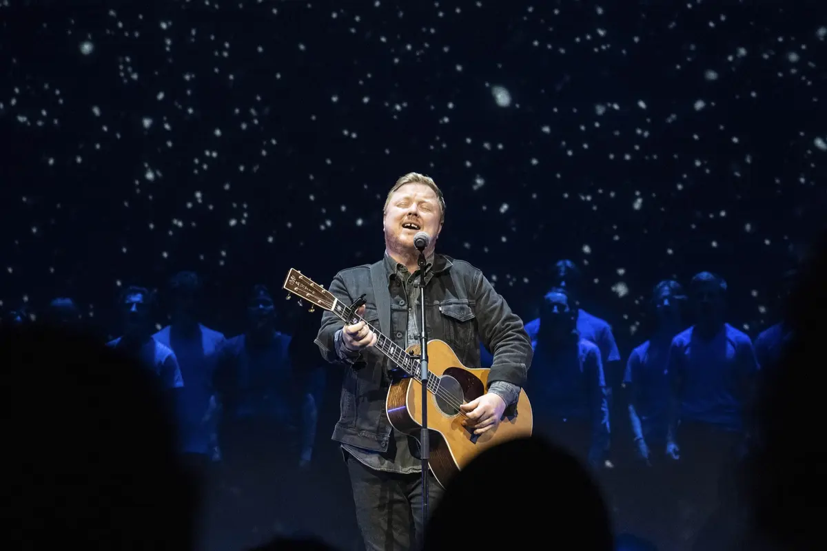Soloist singing with a guitar in front of the star curtain, seen over the heads of the audience