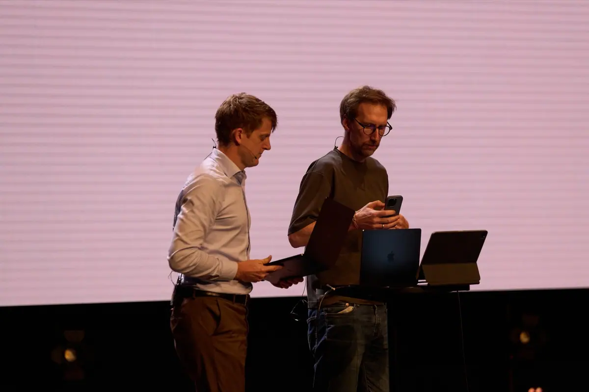 Two hosts preparing with a tablet and laptop on stage
