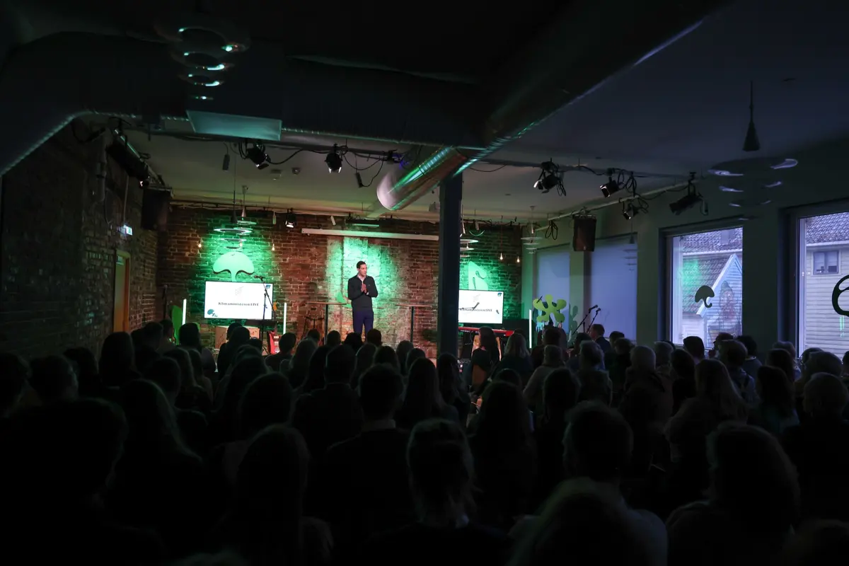 Dark hall with a large audience watching a speaker on stage