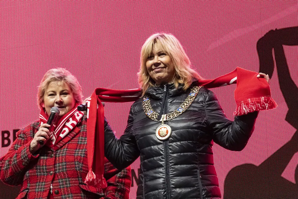 Two women on stage, one wearing a mayoral chain, holding up a Brann scarf