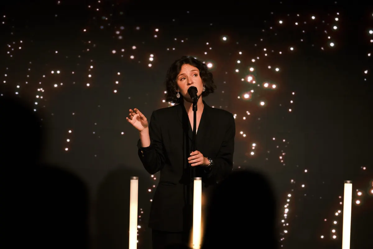 Woman speaking into a microphone in front of a dark starry backdrop