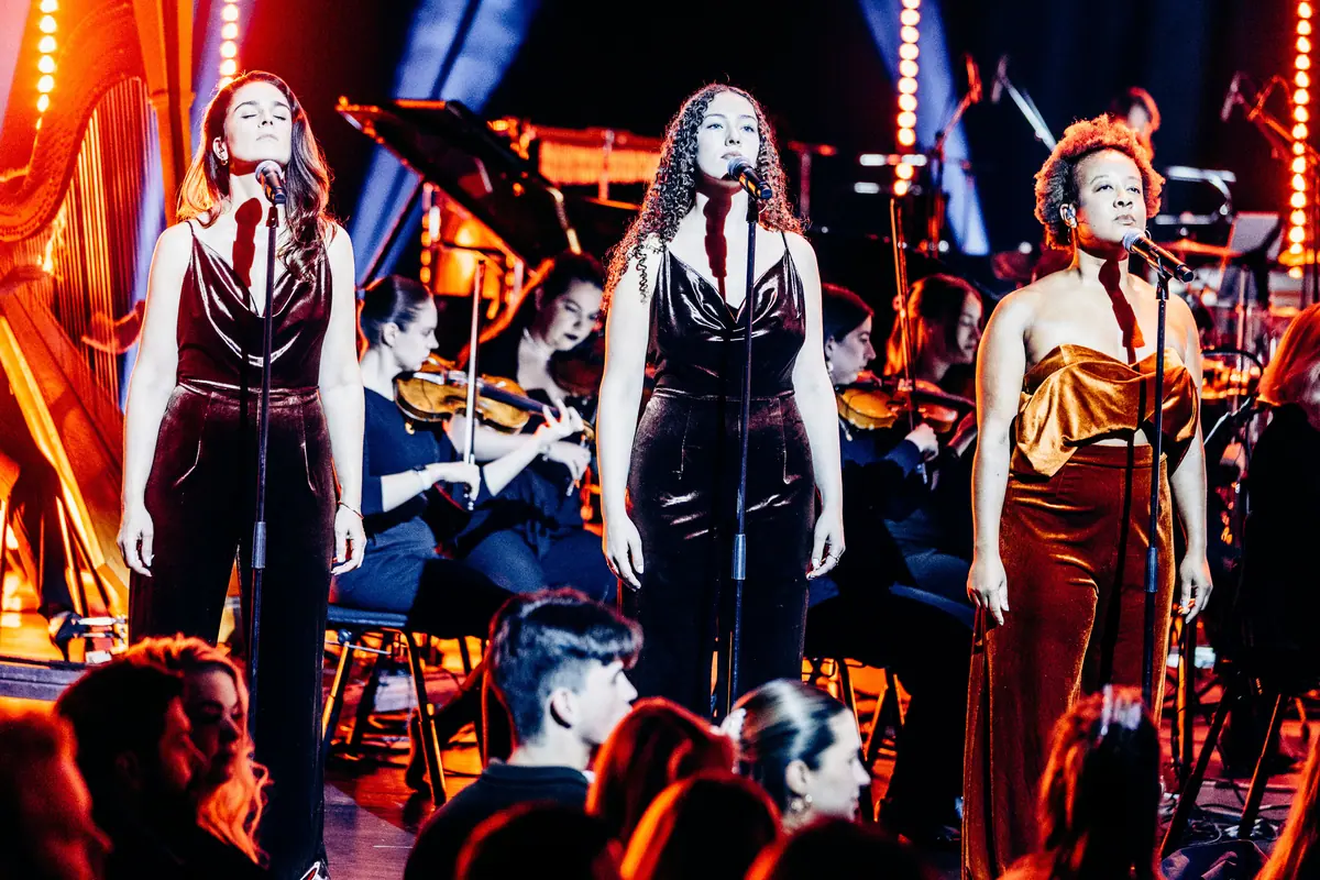 Three vocalists in velvet dresses singing before the orchestra at Red Bull Symphonic