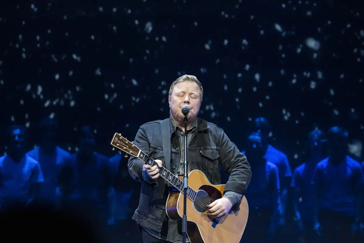 Soloist with guitar before a starry curtain, with the choir behind it in Grieghallen