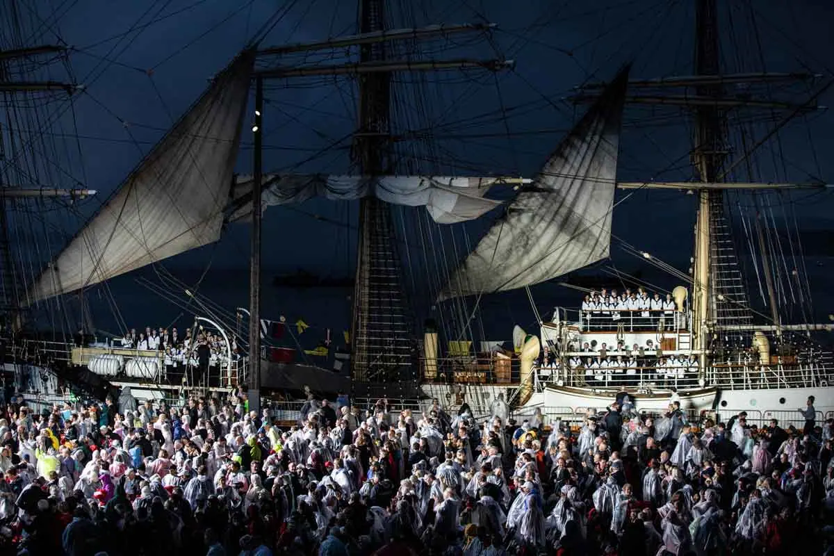 Audience in rain ponchos before a tall ship and vessel at night at a Viking christening
