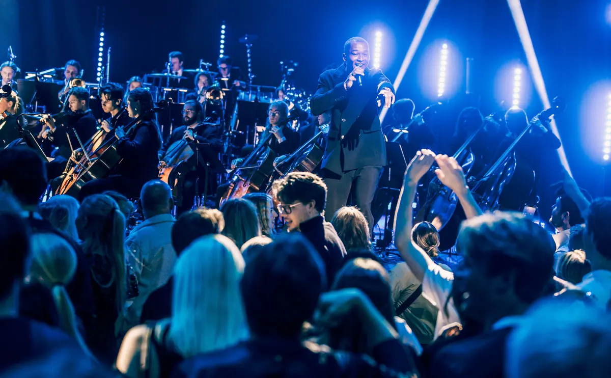 Vocalist and orchestra in blue light as the audience raises their hands