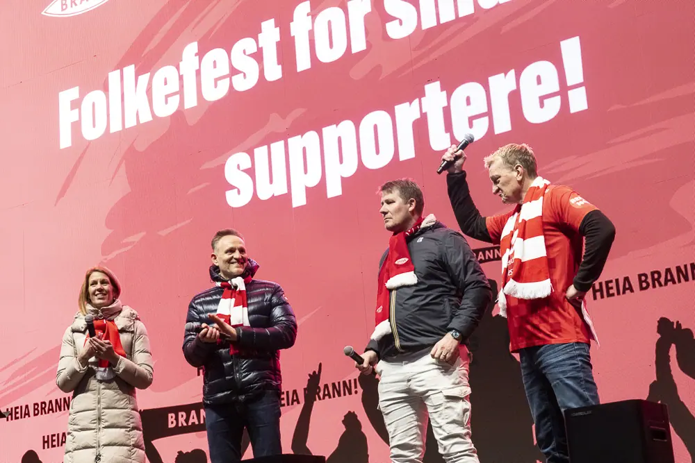 Four people on stage before the «Folkefest for supportere!» banner at the Brann party