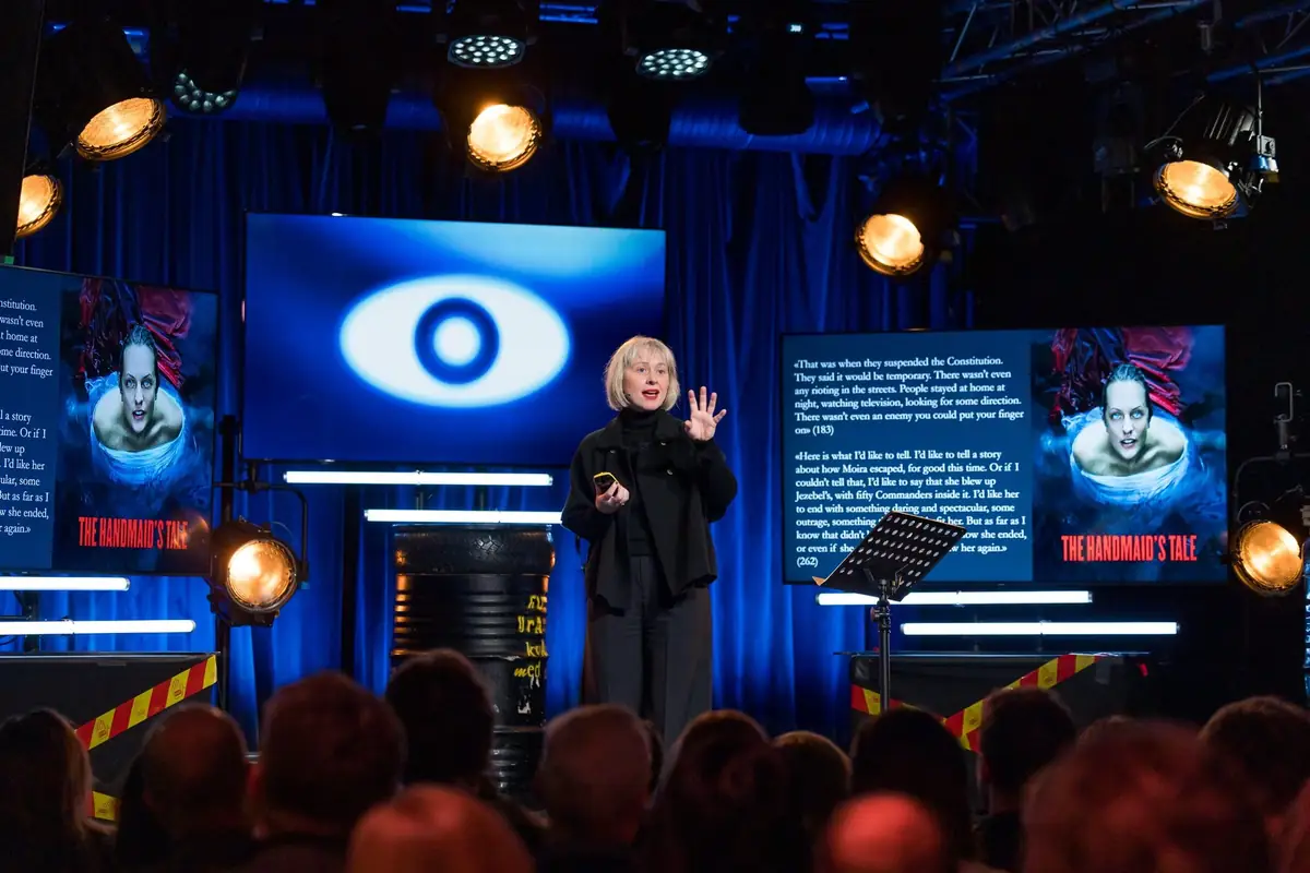 Speaker on stage at Kvarteret with an eye on screen and surveillance-themed set