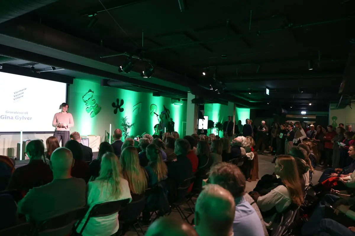Packed hall with the audience facing a green-lit stage at the climate festival
