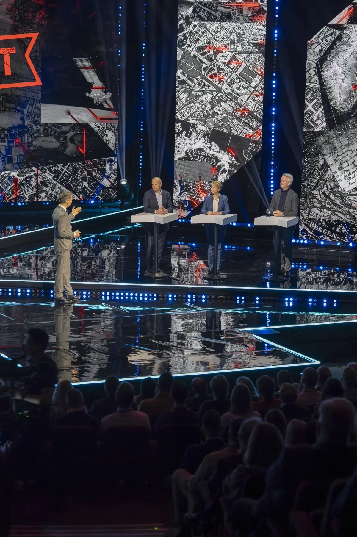 Moderator and three participants at lecterns on stage, with the audience in the foreground