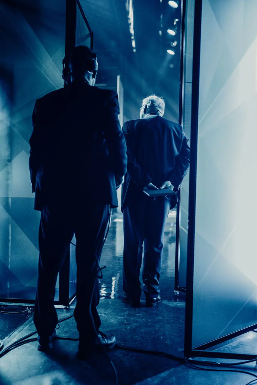 Two silhouetted men looking out at the stage from the wings at Vestlandskonferansen