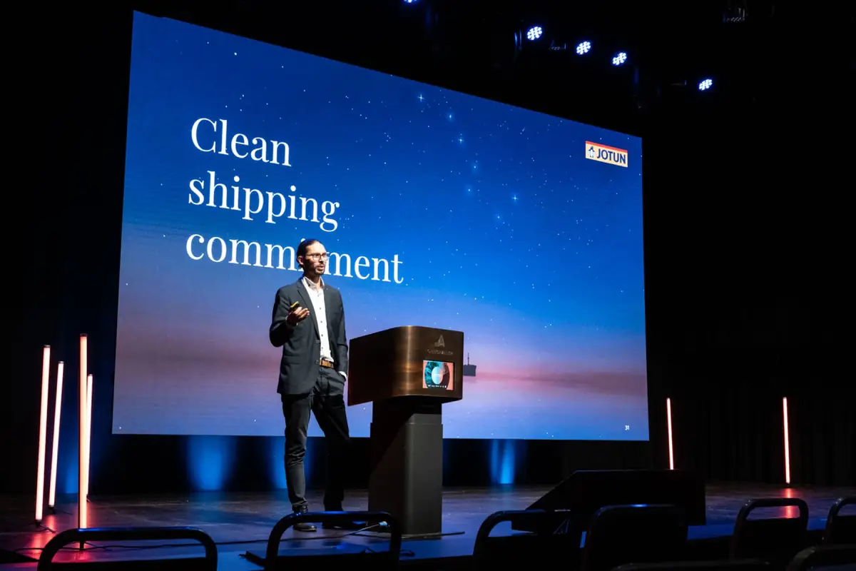 Speaker at a lectern before a large screen reading «Clean shipping commitment»