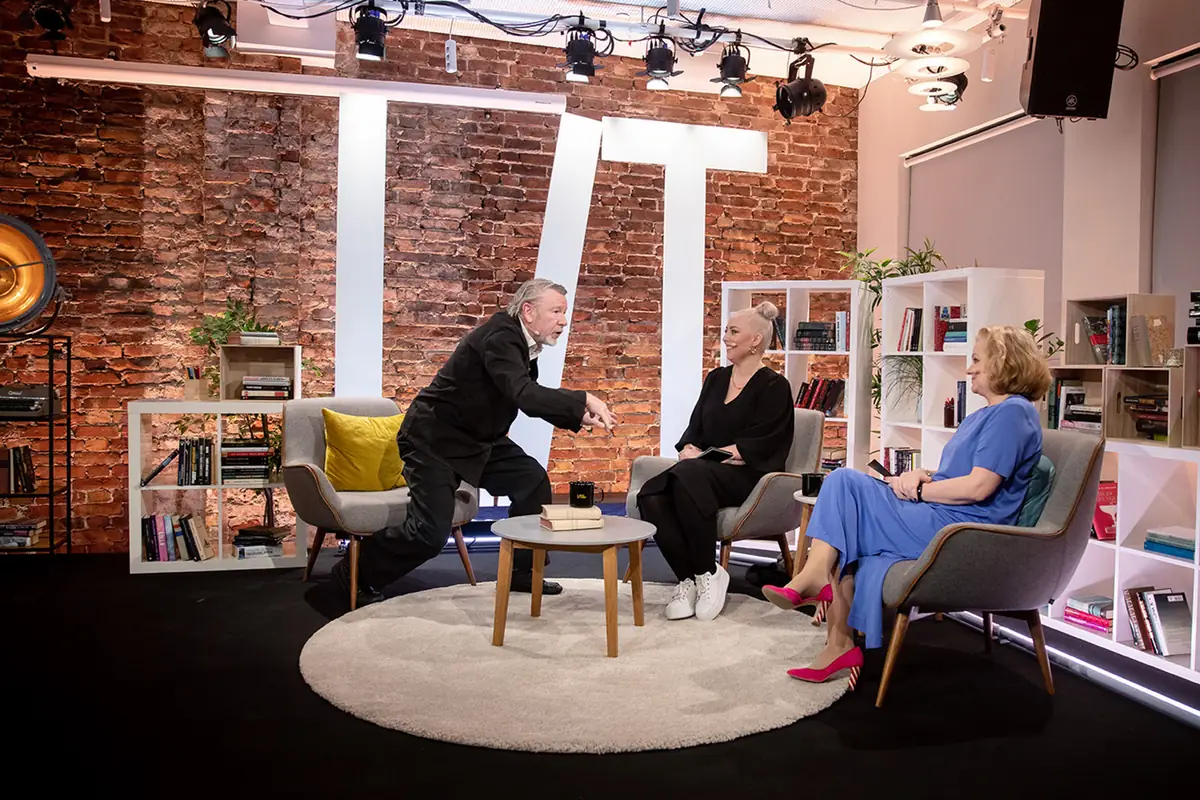 Host and two guests in a lounge set in a brick-walled studio during Literature Live