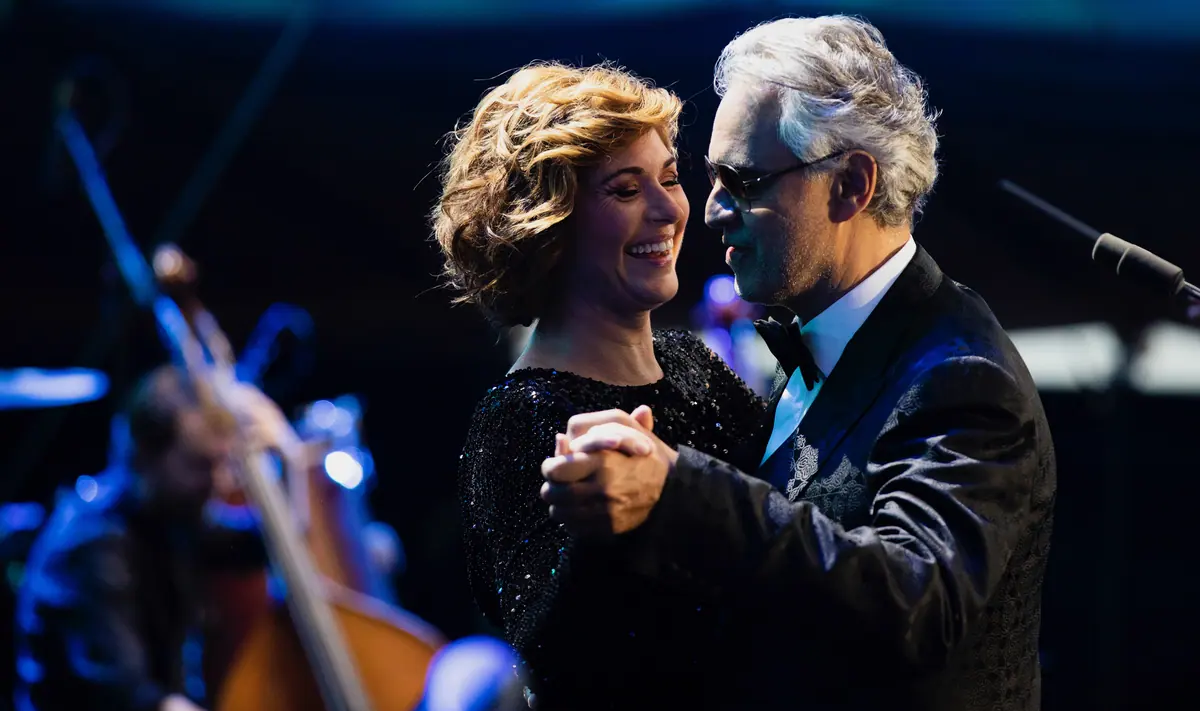 Singing couple in evening wear dancing on stage in front of an orchestra