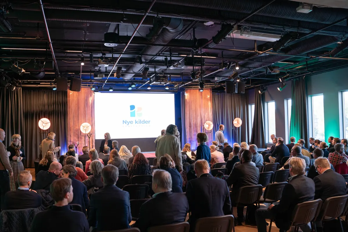 Overview of the conference hall with the audience seated and the Nye kilder logo on screen
