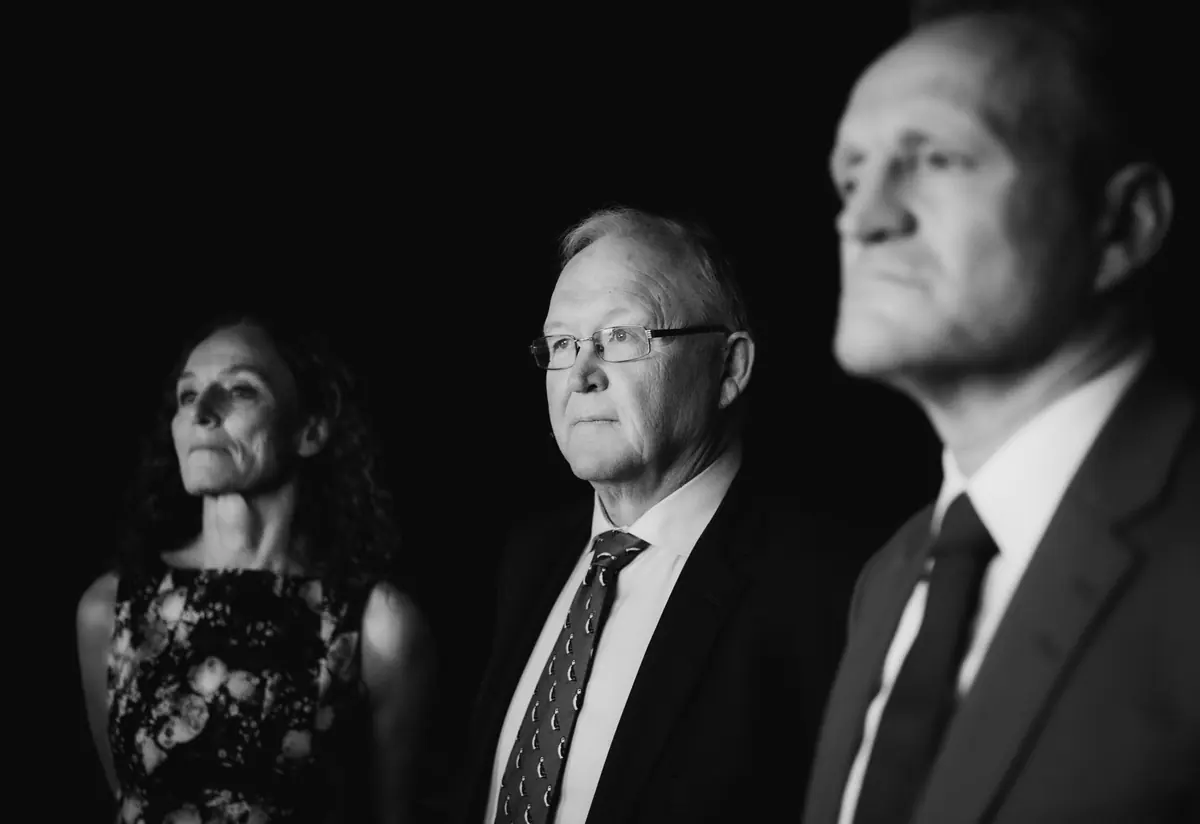 Three audience members watching intently from the hall, black and white