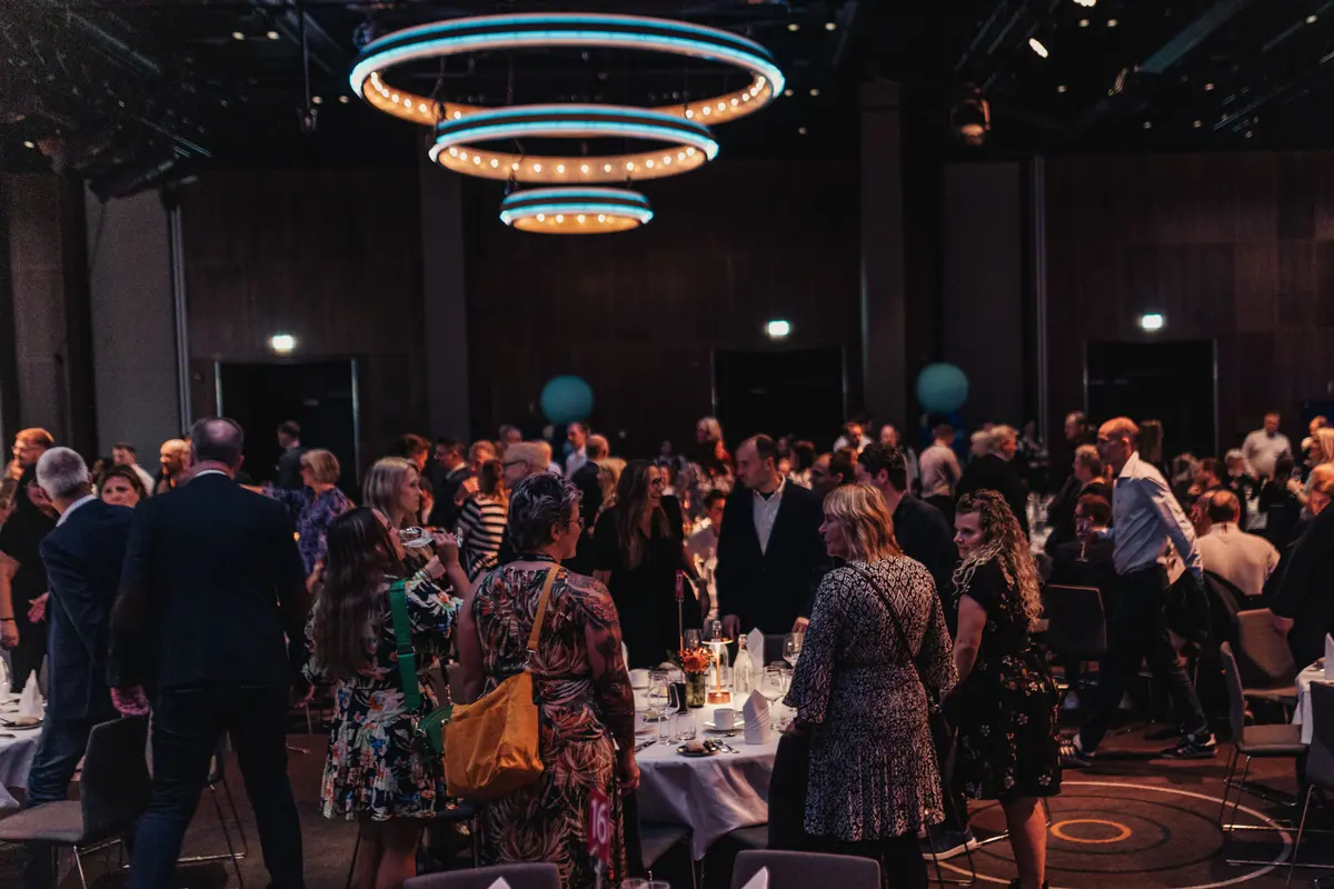 Party guests mingling among dinner tables under ring-shaped chandeliers