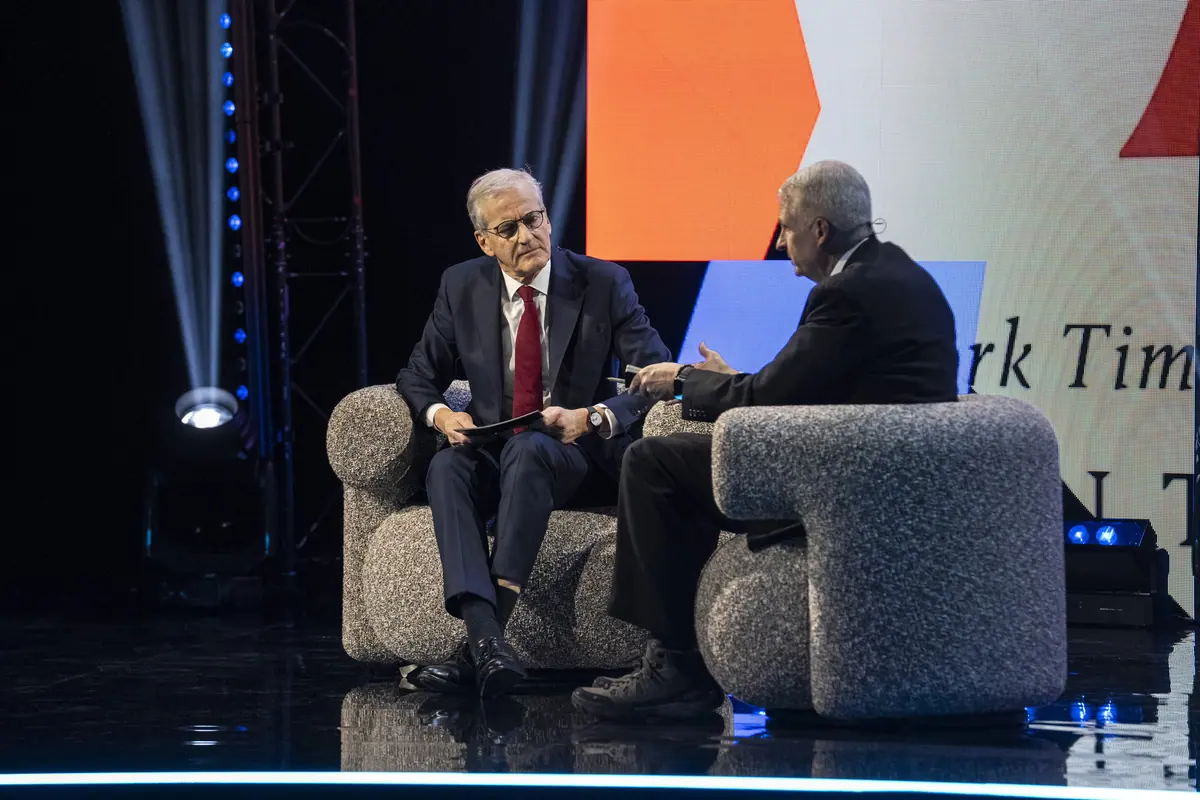 Two men in conversation in armchairs on stage in front of a large screen