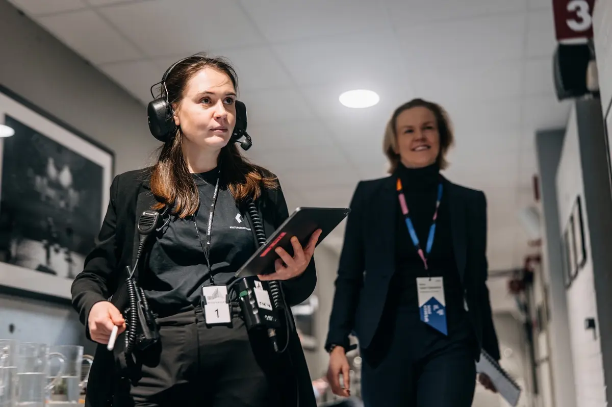 Backstage: two crew members with accreditation in the corridor, one with a headset and tablet
