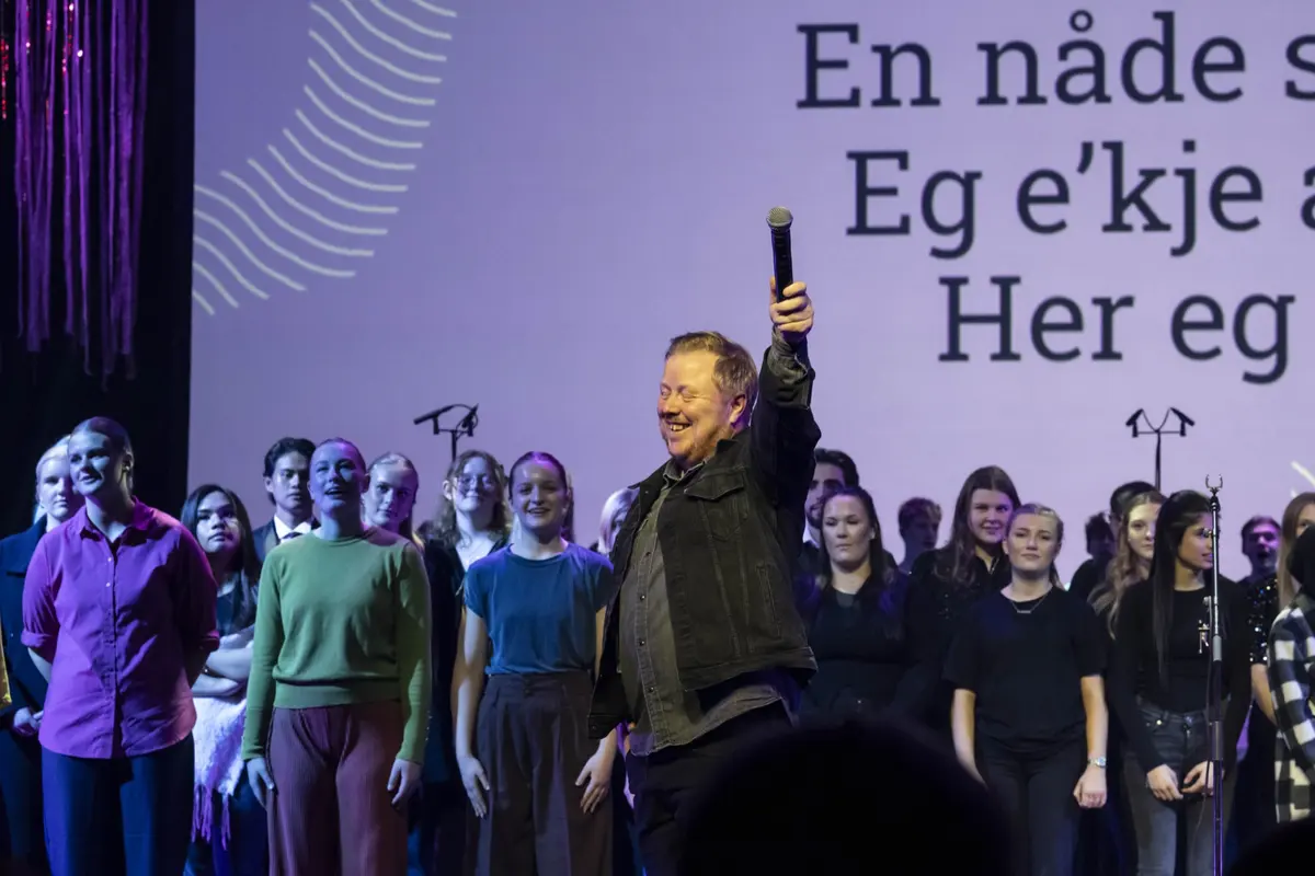 Soloist with a raised microphone together with the youth choir in front of a large text screen