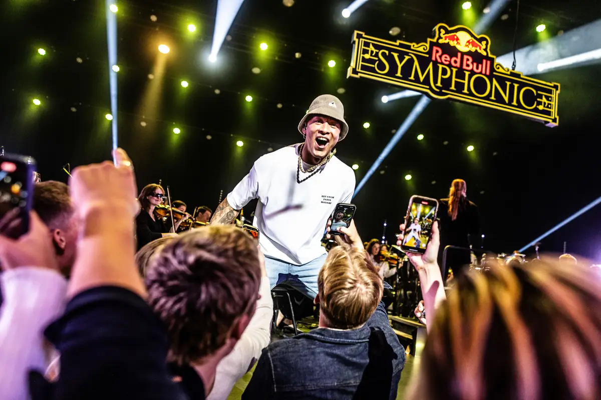 Rapper in a bucket hat on stage among phone-holding fans at Red Bull Symphonic