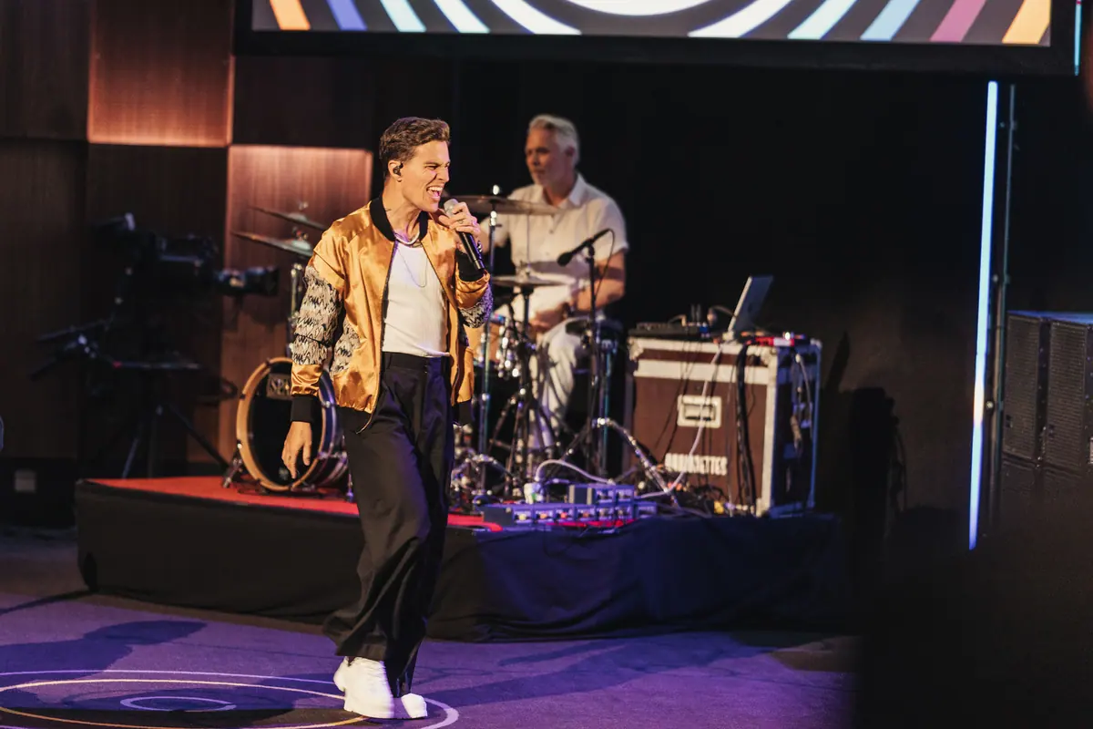 Singer in a gold jacket and drummer on a small stage in purple light