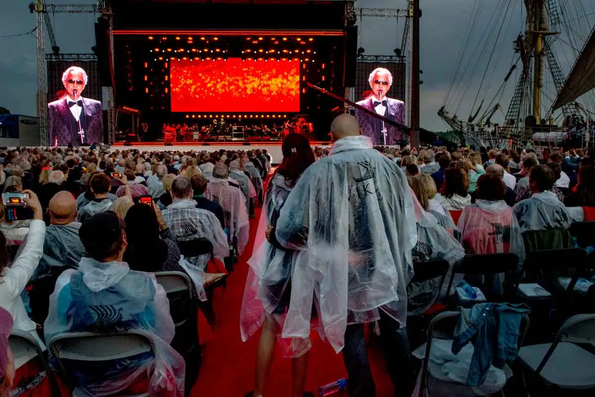 Audience in rain ponchos before an outdoor stage with large screens at a Viking christening